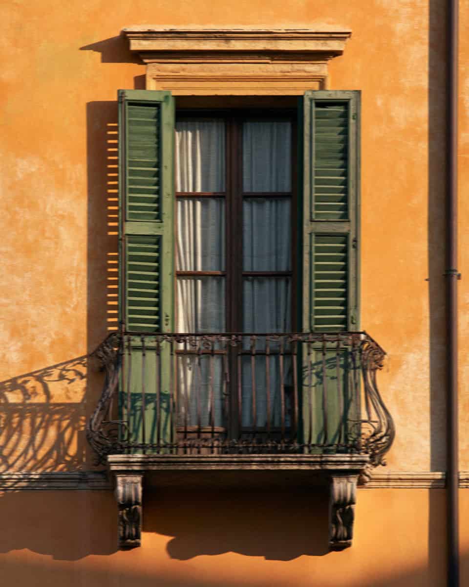 A shuttered window and wrought-iron balcony on an ochre Verona palazzo