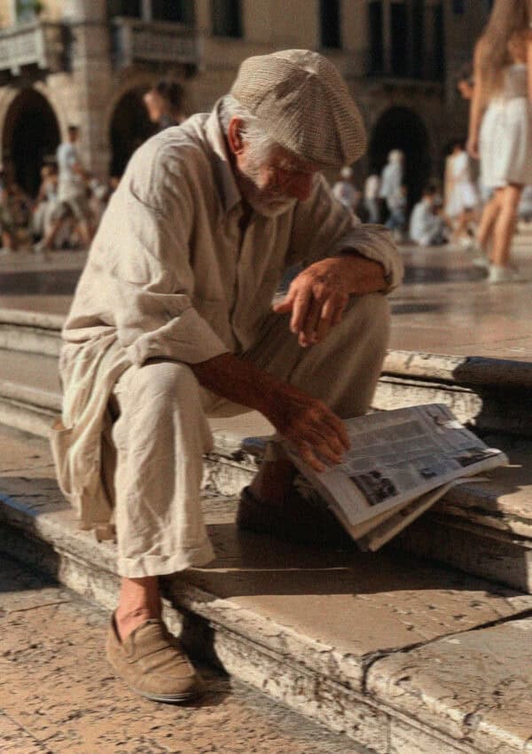 An older man reading a newspaper on the steps of a Verona piazza