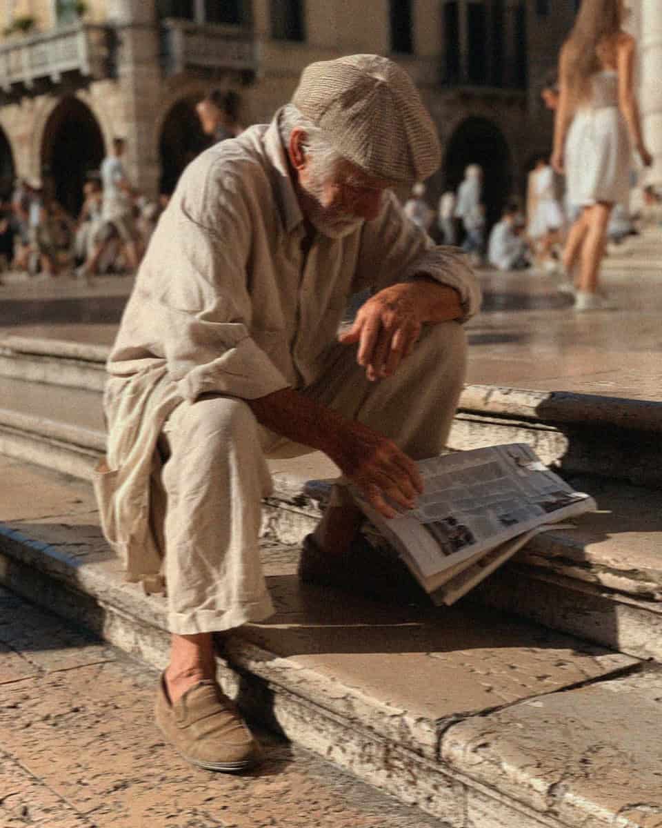 An older man reading a newspaper on the steps of a Verona piazza