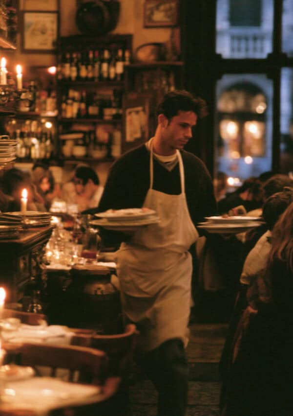 A waiter carrying plates through a candlelit Verona osteria