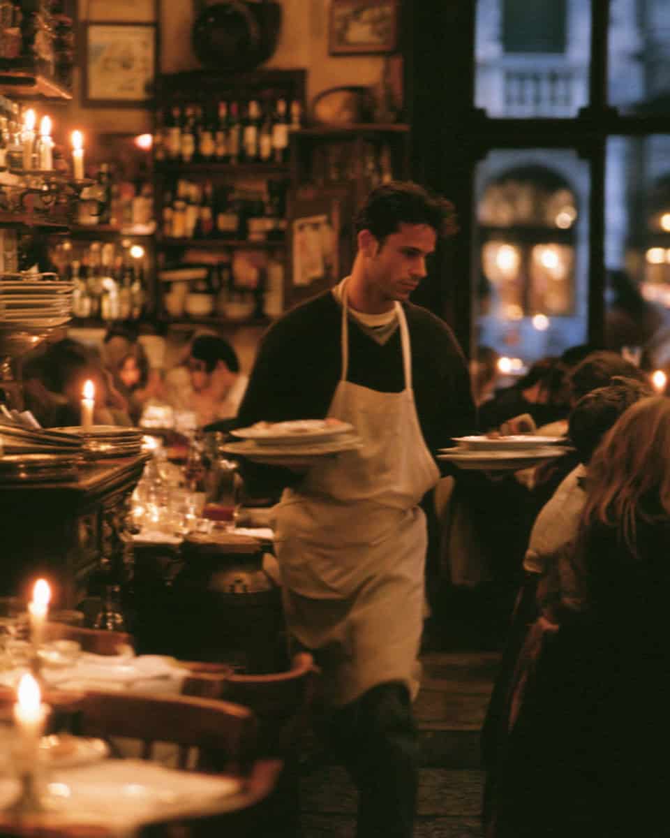 A waiter carrying plates through a candlelit Verona osteria