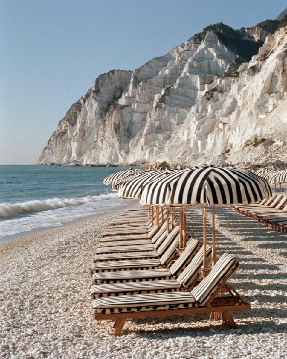 Ranked rows of striped umbrellas and wooden loungers on a Versilia beach in Tuscany below white quarried cliffs, no people