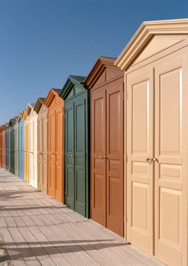 A row of painted wooden changing cabins in pink, green and terracotta along a boardwalk at a beach club on the Versilia coast in Tuscany, no people