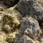 Close-up of yellow sulphur crust and grey volcanic rock at the crater rim on Vesuvius in hard clear light