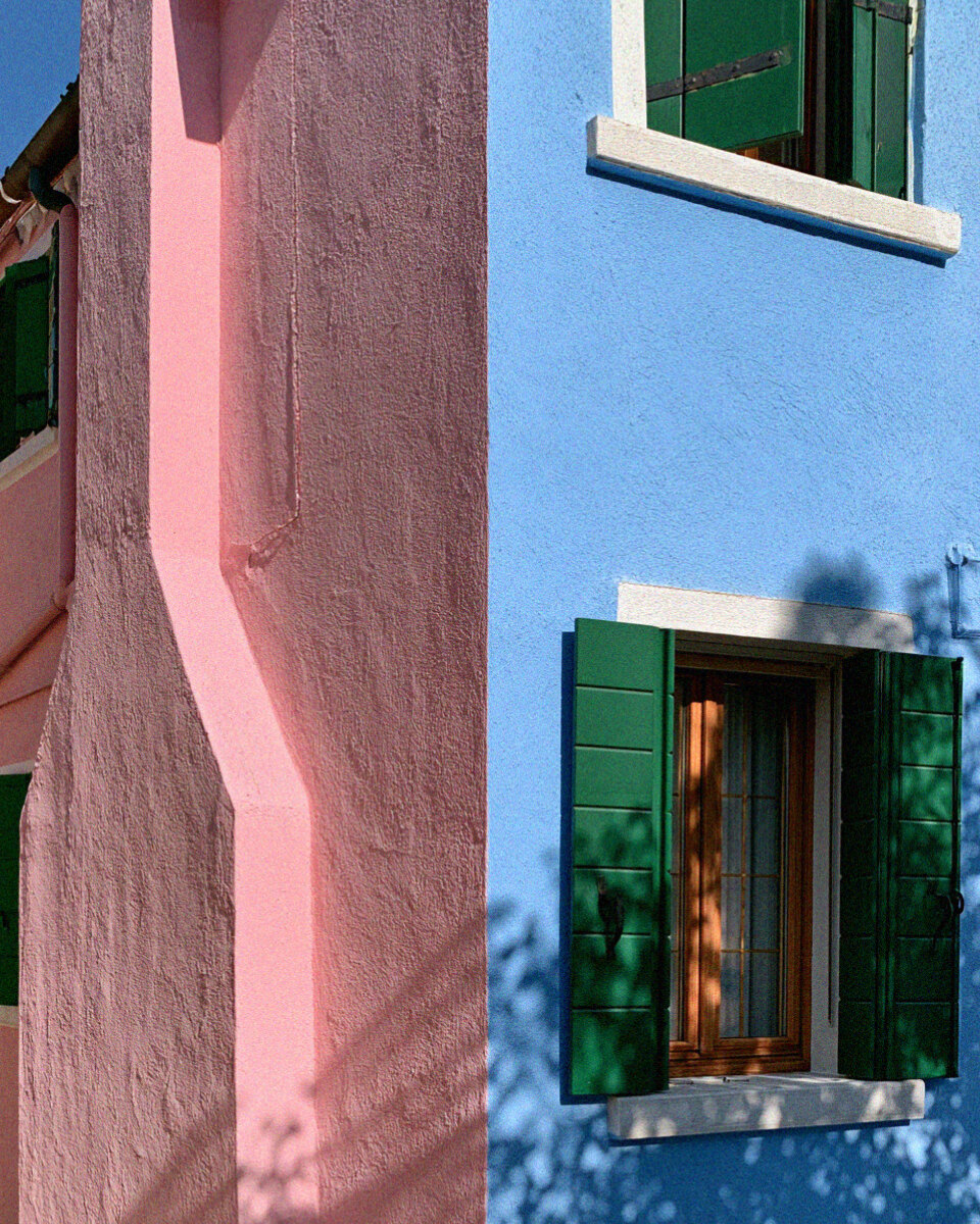 Victoria van der Berg in a green dress at the prow of a boat on a Burano canal lined with coloured houses.