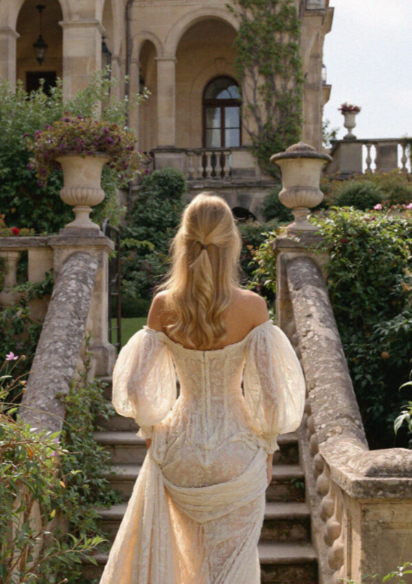 Victoria van der Berg in an off-shoulder lace wedding gown descending the stone garden steps of a villa on Lake Como