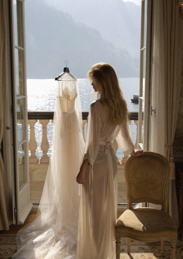 A wedding gown hanging by an open window over Lake Como with Victoria van der Berg looking at it