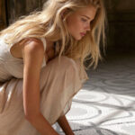 Victoria van der Berg in a cream dress on a mosaic floor in Pompeii with strong light and shadow falling across the pattern