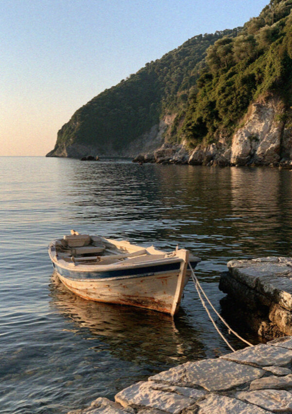 An empty pebble cove on the northeast coast of Corfu with a single moored boat in late afternoon light