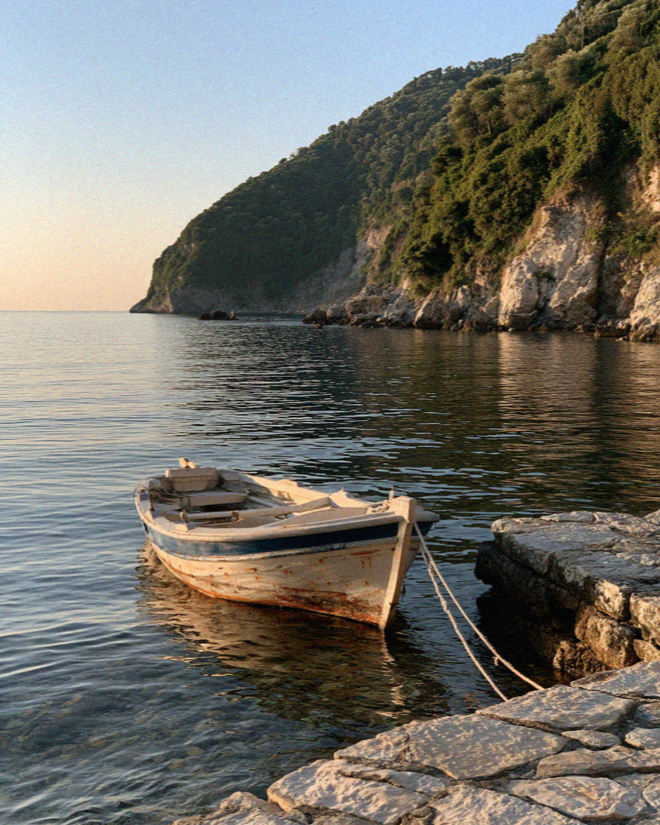 An empty pebble cove on the northeast coast of Corfu with a single moored boat in late afternoon light