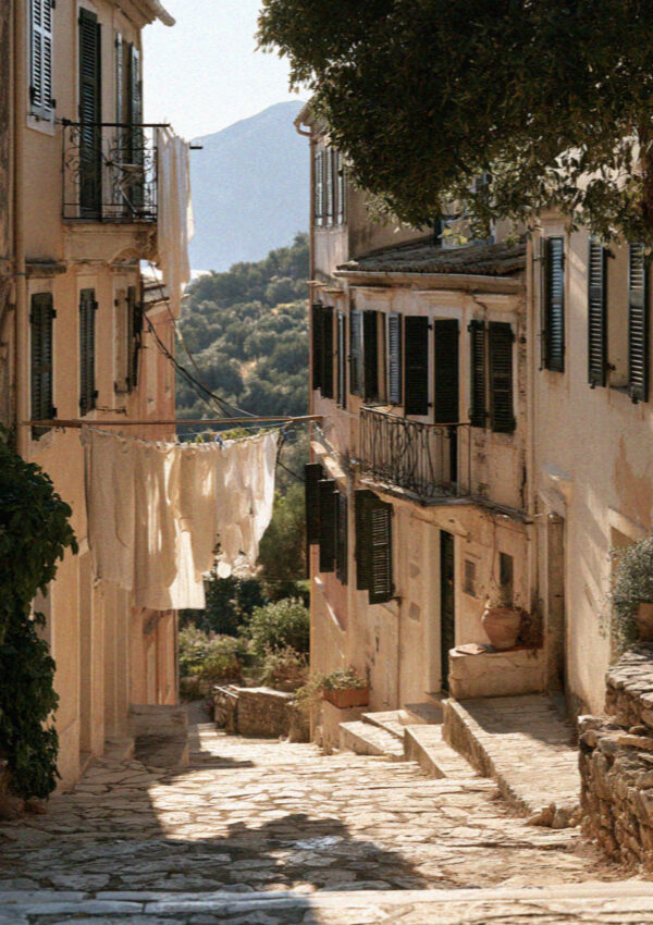 A quiet lane of tall shuttered houses in Corfu with the hills showing at the end of it