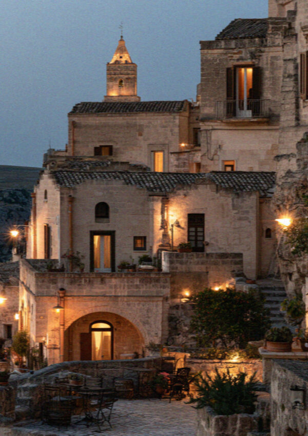 The stacked rooftops of Matera as the first lights come on at dusk