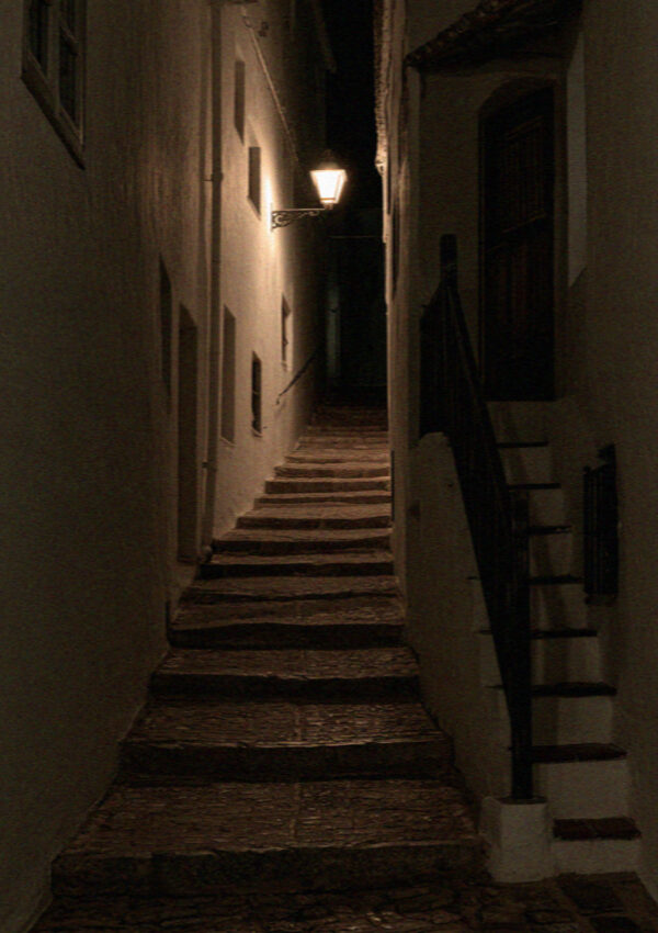 A narrow whitewashed stepped lane in Mykonos lit by a wall lantern at night