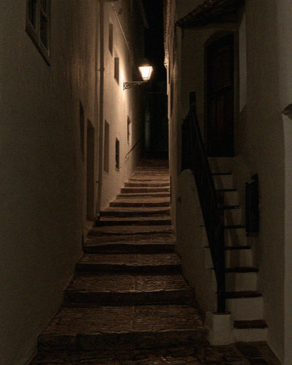 A narrow whitewashed stepped lane in Mykonos lit by a wall lantern at night