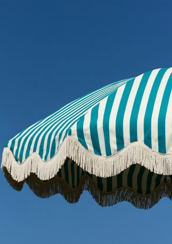A turquoise and white fringed beach umbrella against a deep blue Mykonos sky
