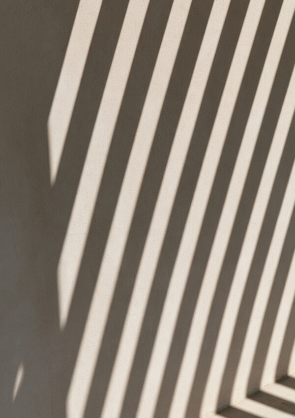 Hard striped shade falling across a pale Mykonos wall