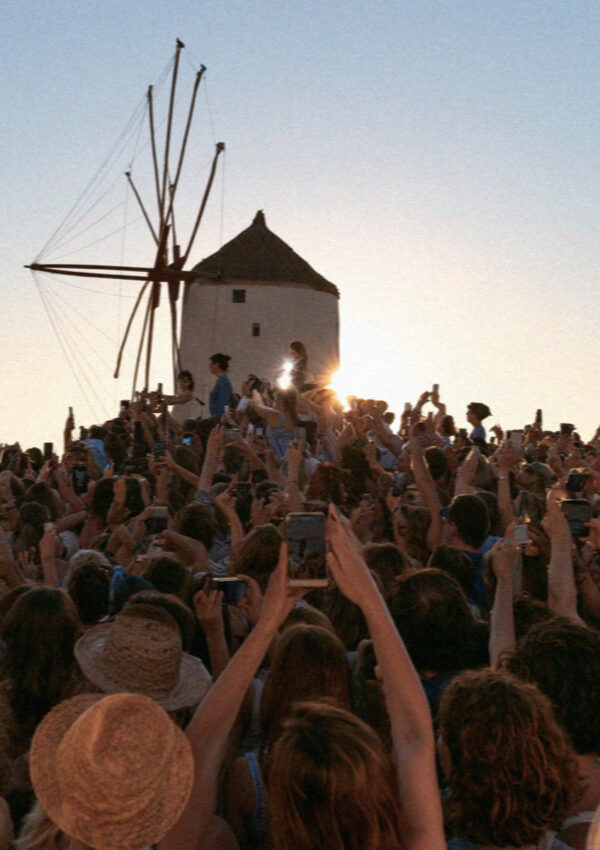 A crowd with raised phones photographing the windmills at sunset in Mykonos