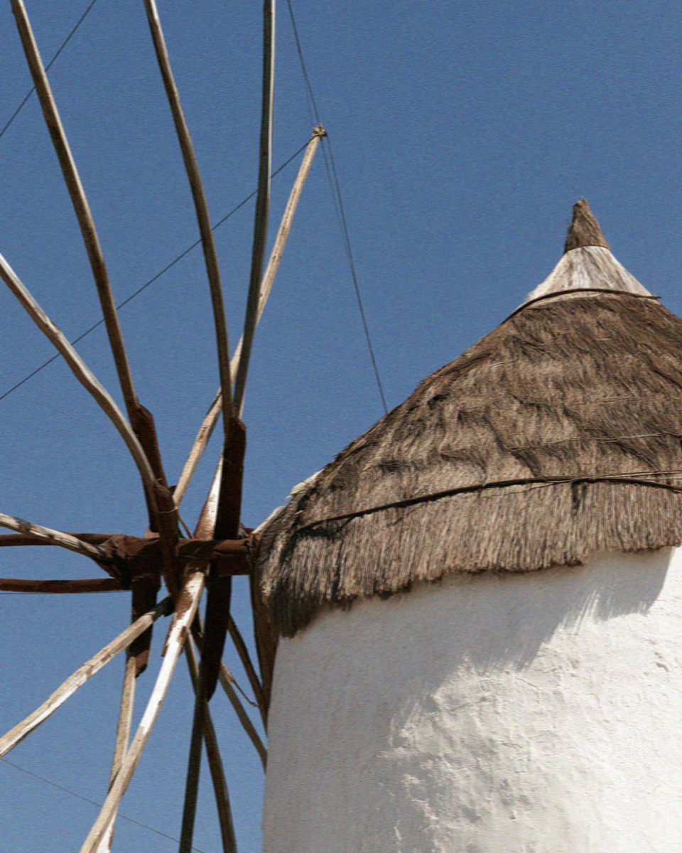 Close detail of a thatched windmill cap and wooden vanes against a blue sky in Mykonos