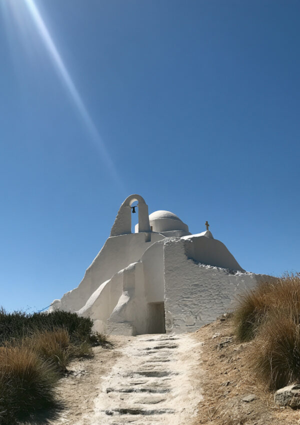 A whitewashed Cycladic chapel with an arched bell tower above a stone path on Mykonos