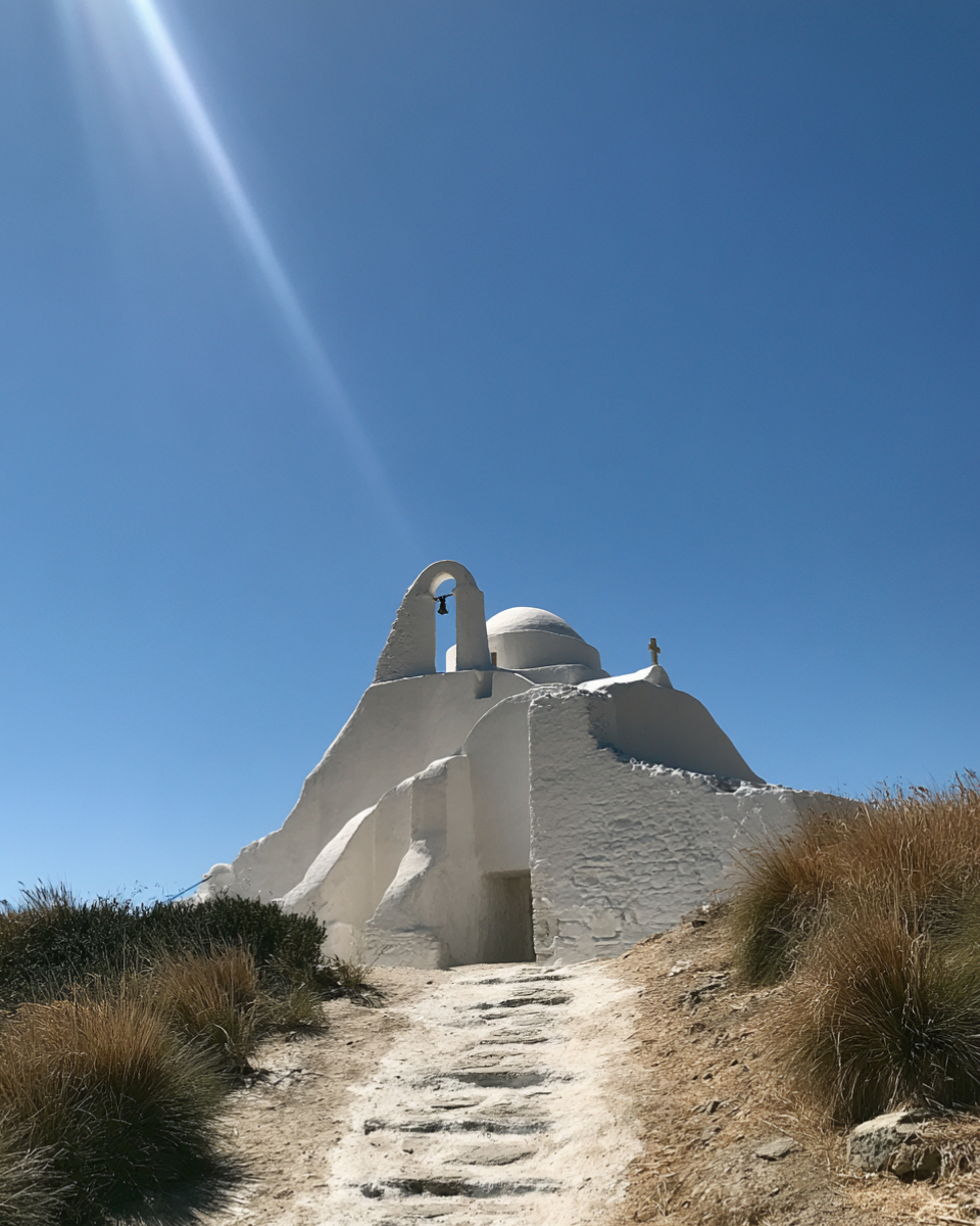 A whitewashed Cycladic chapel with an arched bell tower above a stone path on Mykonos