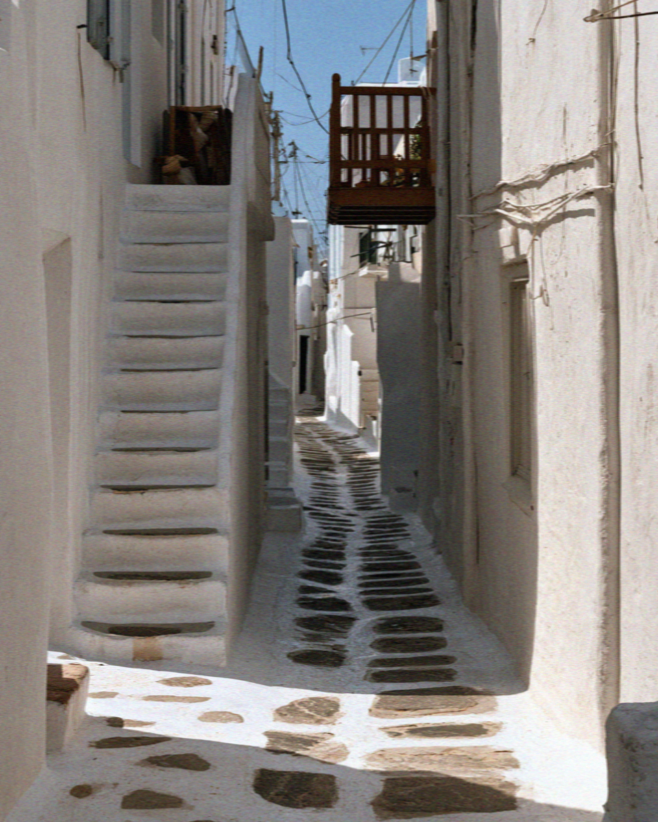 A narrow Mykonos lane with whitewash painted over the flagstone paving and a white outdoor stair