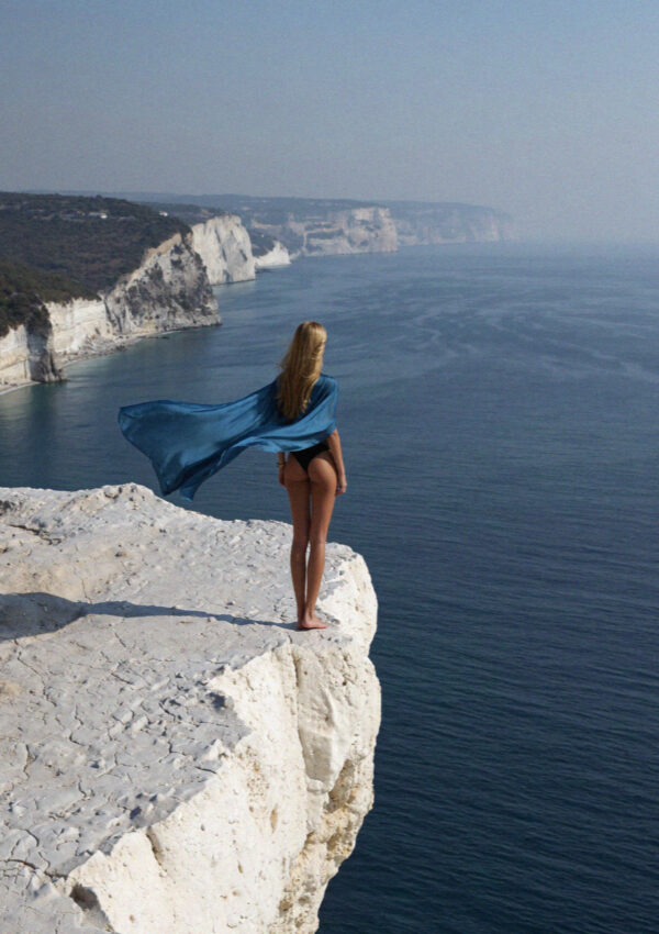 Victoria in a blue gown on a clifftop above the sea in Santorini
