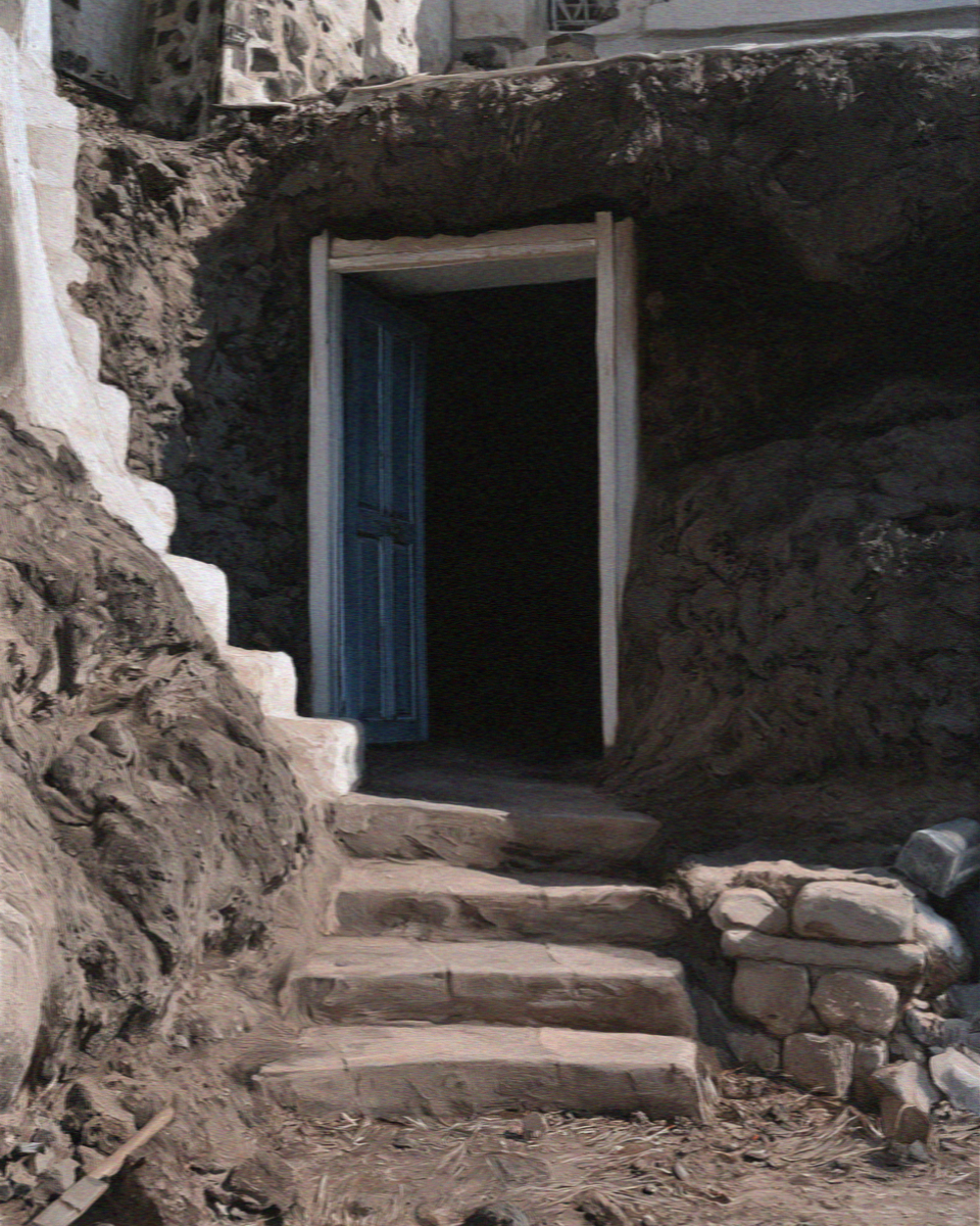 A blue door at the top of stone steps opening into a cave house cut into the rock in Santorini