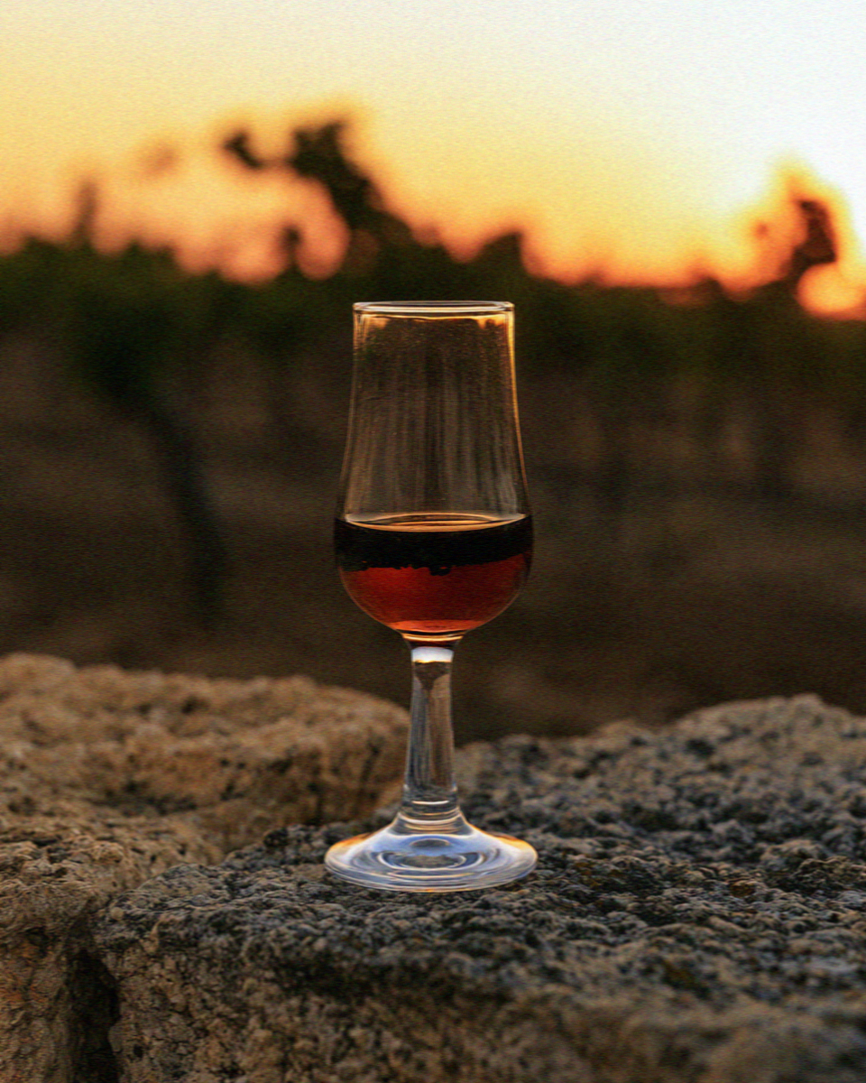 A glass of wine standing on volcanic rock in front of a Santorini vineyard at sunset