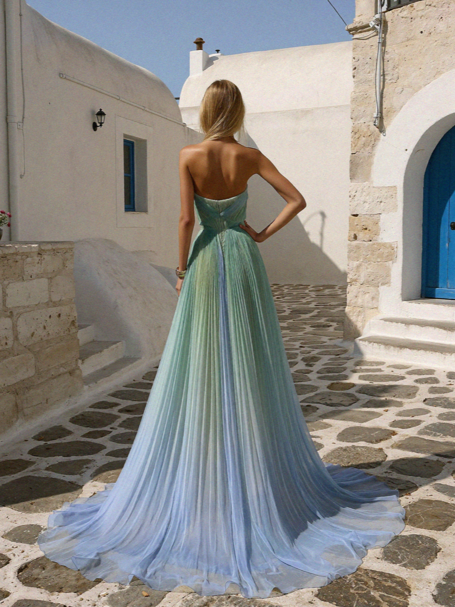Victoria seen from behind in a green and blue pleated gown in a Megalochori lane