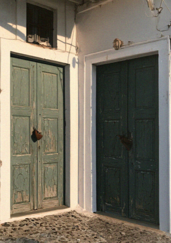 Two old green doors shut and padlocked in a whitewashed village lane in Santorini