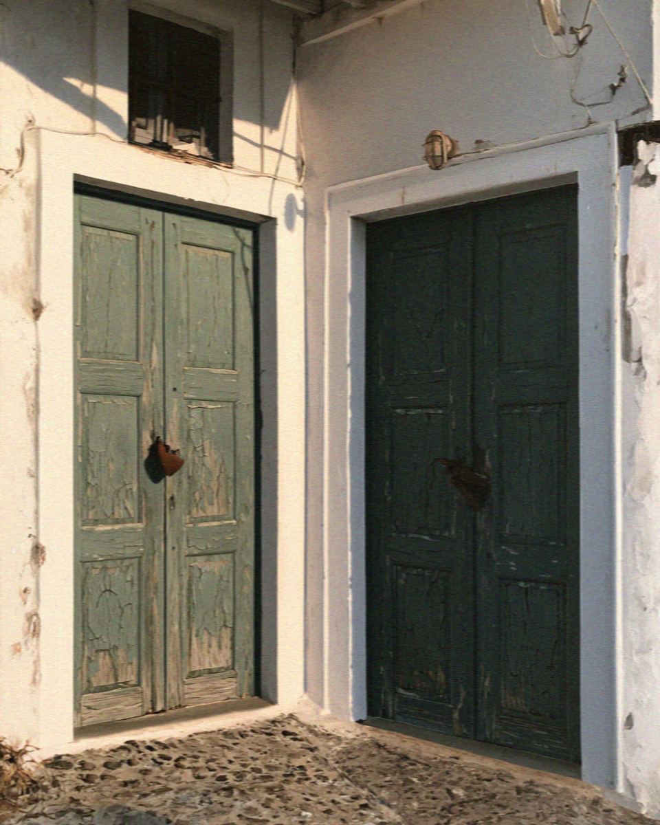 Two old green doors shut and padlocked in a whitewashed village lane in Santorini