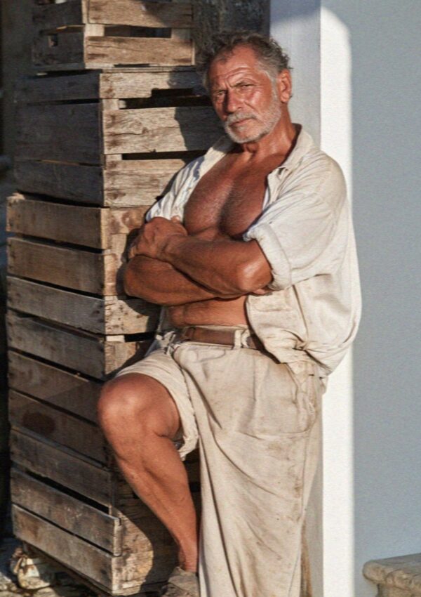An older man standing against a wooden door early in the morning at Scopello, west of Palermo in Sicily