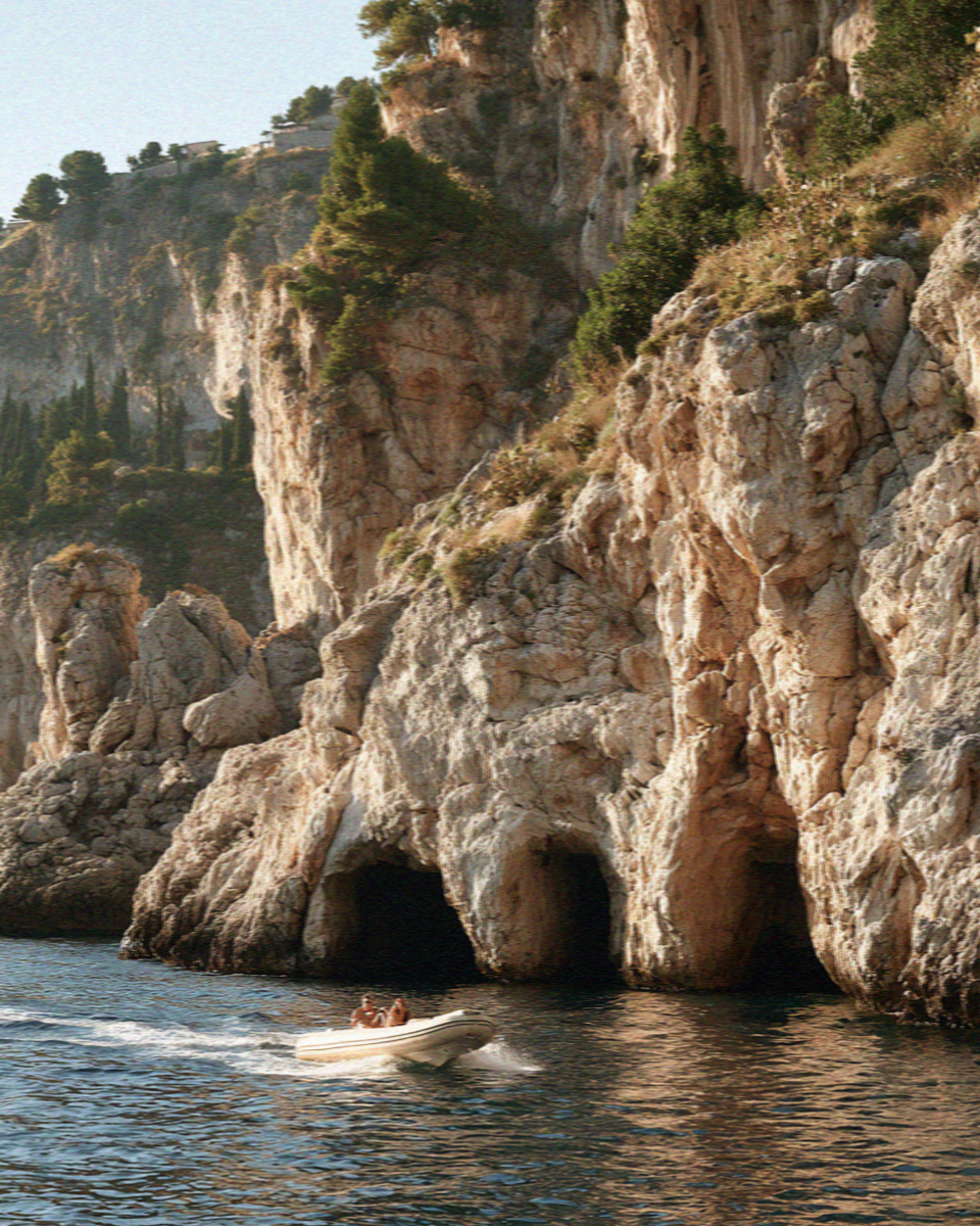 A small boat below the limestone cliffs and grottoes at Taormina in Sicily