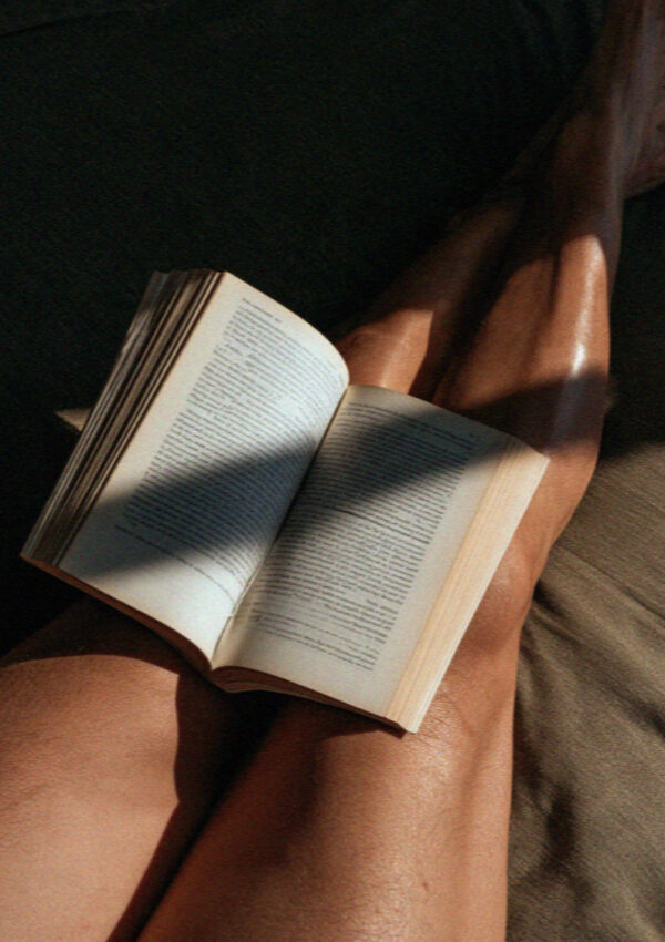 An open book across a lap in hard Mykonos sunlight