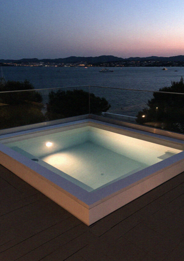 A lit hot tub on a villa terrace above the bay at dusk on Mykonos