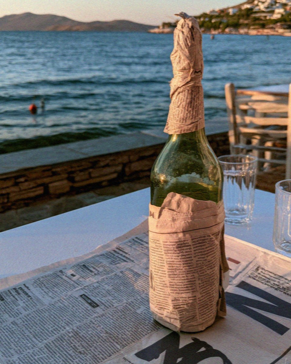 A bottle of green kitron wrapped in newspaper on a cafe table by the harbour on Naxos