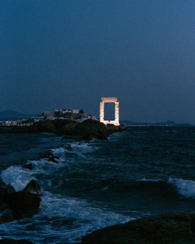 The Portara of Naxos lit at night across dark water from the waterfront