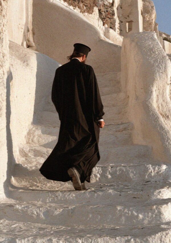 A priest in a black cassock climbing whitewashed steps in Pyrgos on Santorini