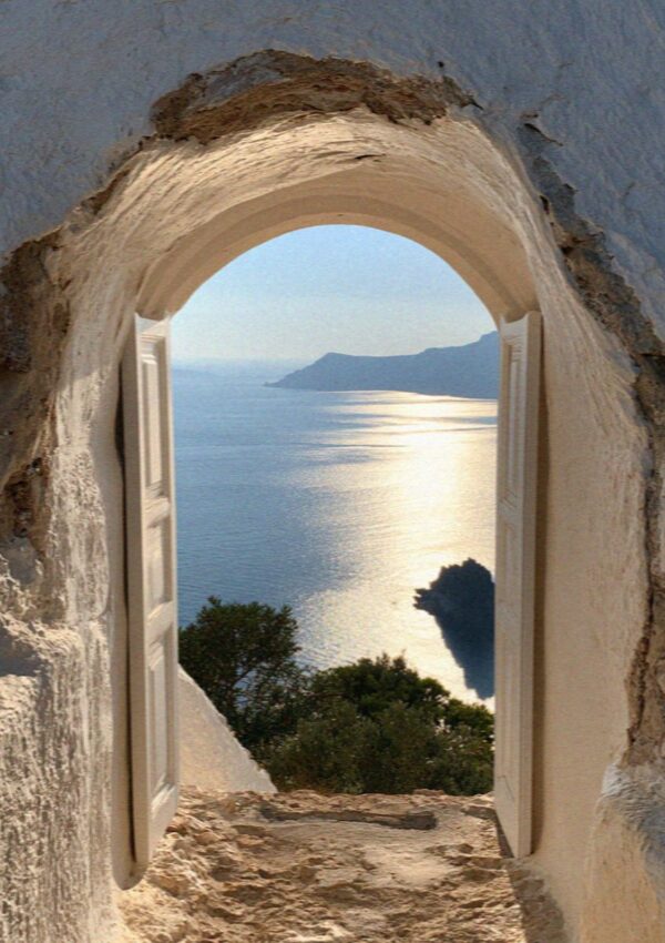 An arched doorway cut into whitewashed rock opening onto the caldera and the sea on Santorini