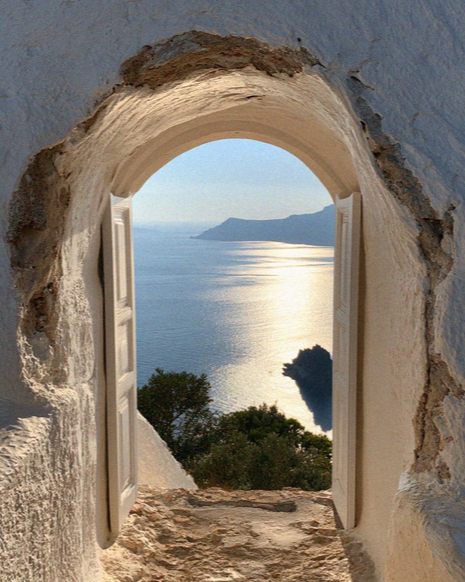 An arched doorway cut into whitewashed rock opening onto the caldera and the sea on Santorini