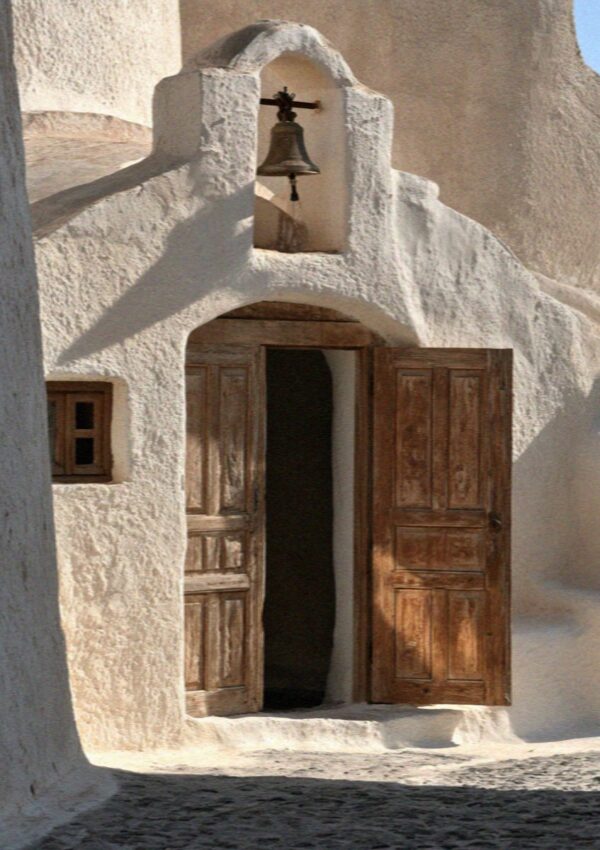 A small whitewashed chapel with a bell and wooden doors inside the kasteli walls of Pyrgos on Santorini