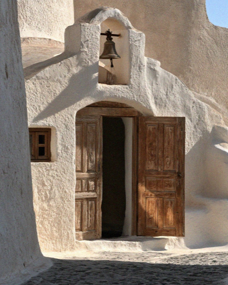 A small whitewashed chapel with a bell and wooden doors inside the kasteli walls of Pyrgos on Santorini