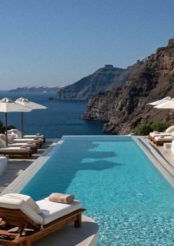 An infinity pool with white loungers and parasols above the caldera on Santorini