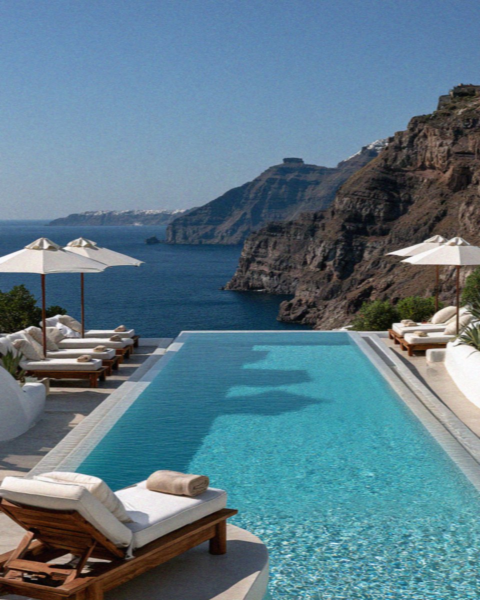 An infinity pool with white loungers and parasols above the caldera on Santorini