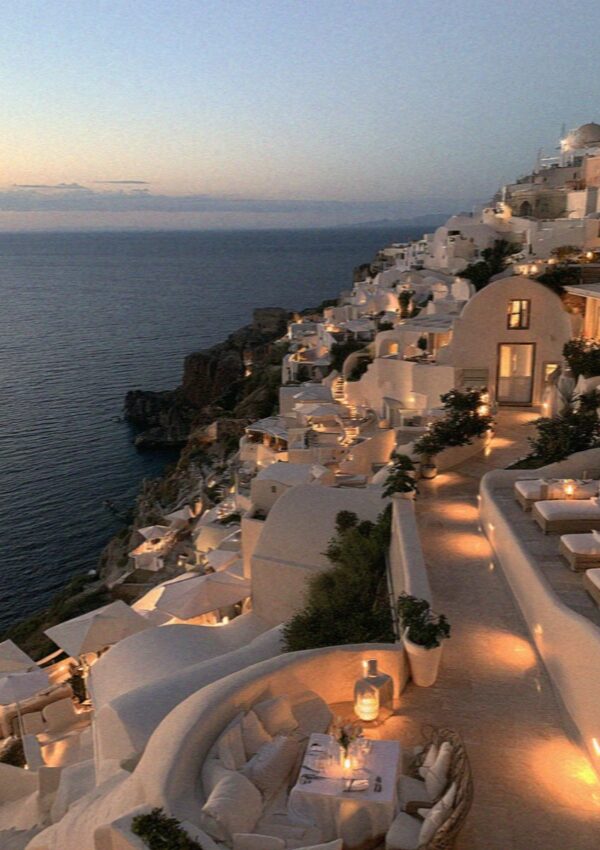 Lamps lit along the whitewashed cliffside terraces of Santorini at blue hour