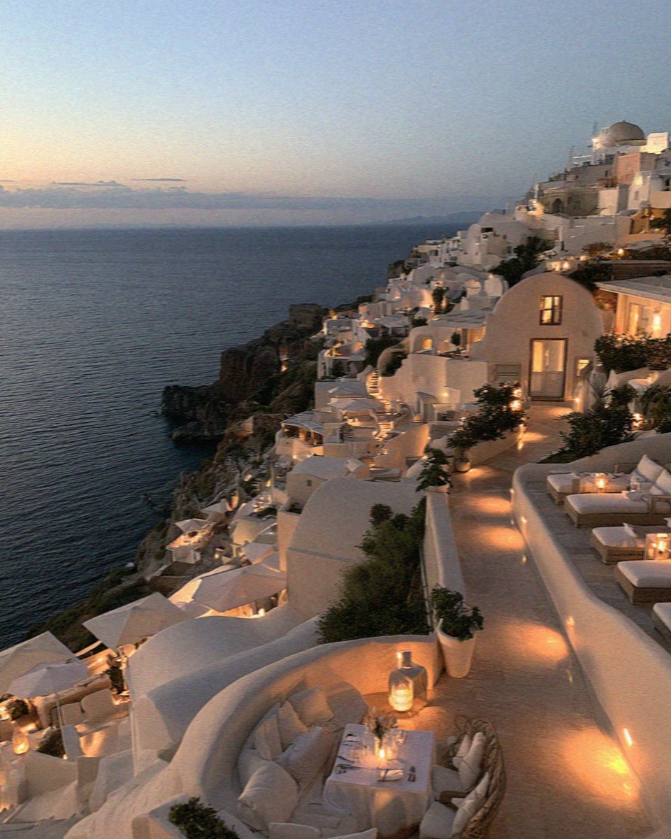 Lamps lit along the whitewashed cliffside terraces of Santorini at blue hour