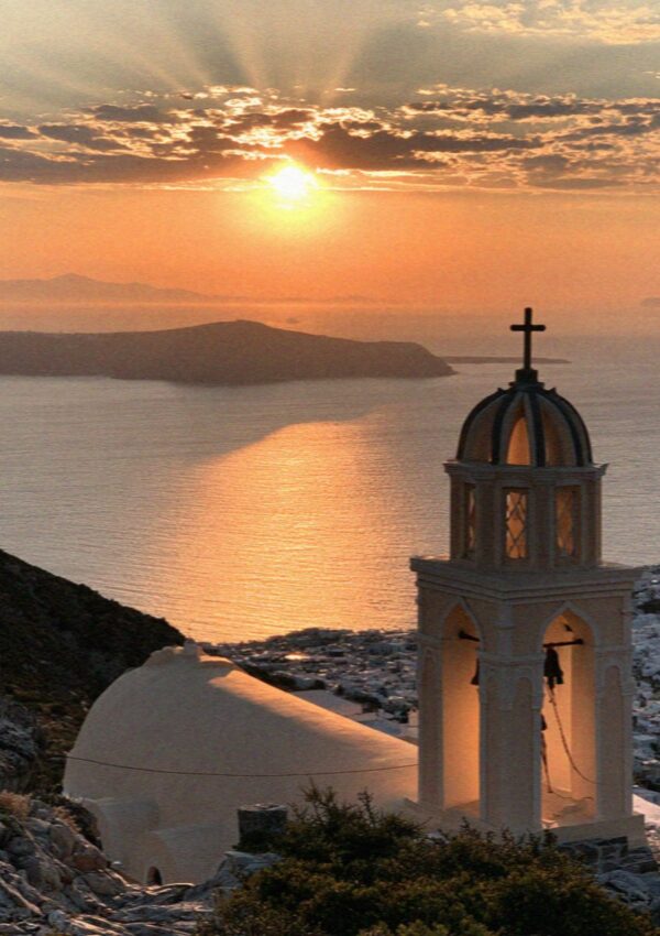 The sun setting over the sea behind a church bell tower in Pyrgos on Santorini