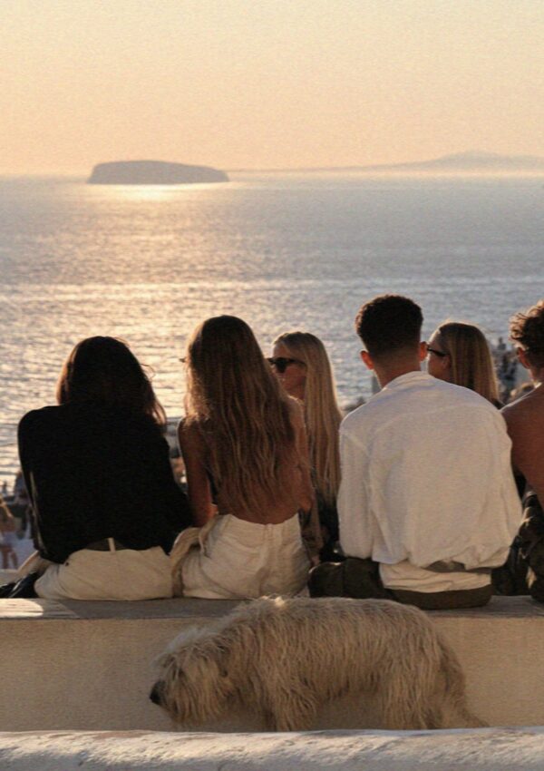 People and a dog sitting on a low wall at the top of Pyrgos watching the sunset over Santorini