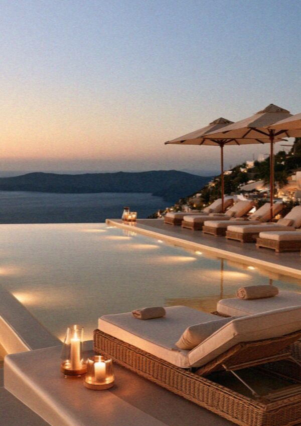 An infinity pool with loungers and candles turning gold at sunset above the caldera on Santorini