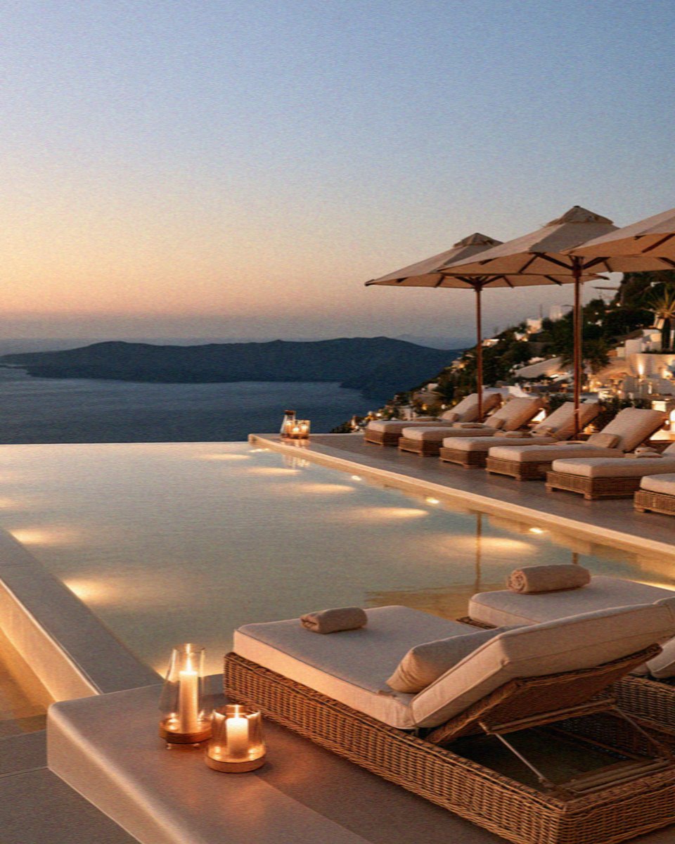 An infinity pool with loungers and candles turning gold at sunset above the caldera on Santorini
